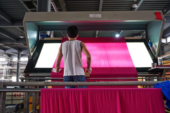A worker inspects newly dyed pink fabric for inconsistencies and holes